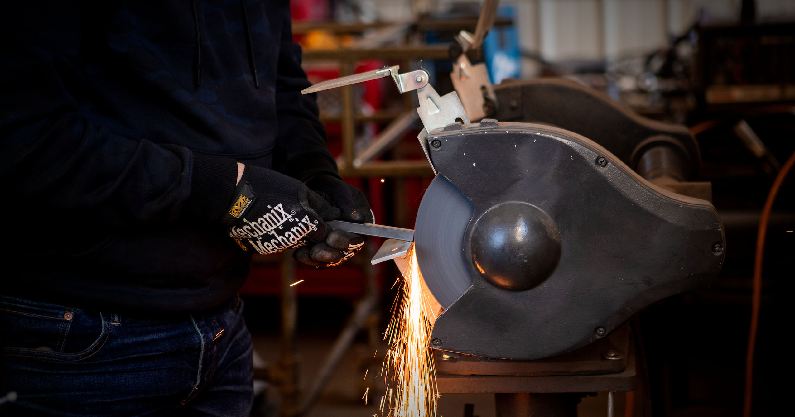 Close-up of a person using a grinding machine on a metal piece, with sparks flying in a workshop.